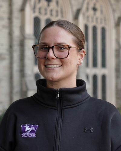 A female student smiling inside of a building with a black Western sweater on