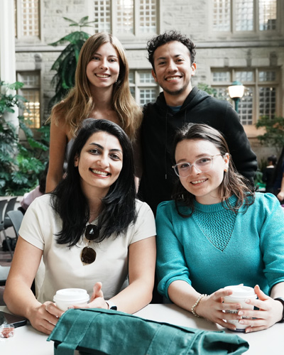 4 students standing and smiling while drinking coffee