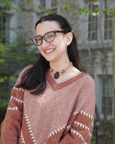 A student with black hair smiling in front of a building
