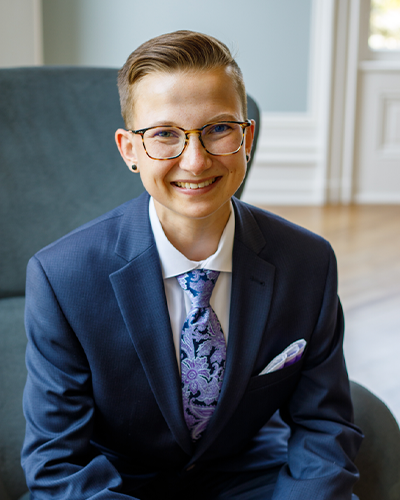 Leighton Schreyer wearing a blue suit leaning forward in chair smiling