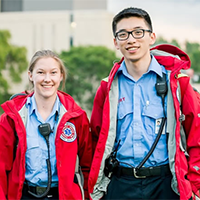 two SERT members wearing blue button down shirts and red SERT jackets with handheld speaker microphones attached to their shirt collars