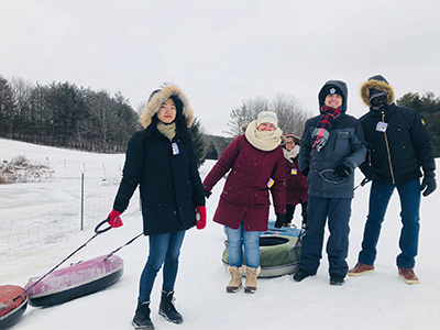Students dressed in warm gear pulling snow tubes up the hill and smiling.